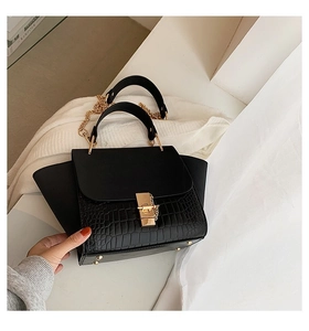 Close-up of black matte and crocodile texture leather bag with golden chain and lock