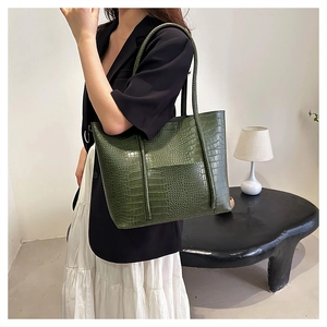 Dark green tote bag with crocodile texture worn by a model in a minimalist studio setting