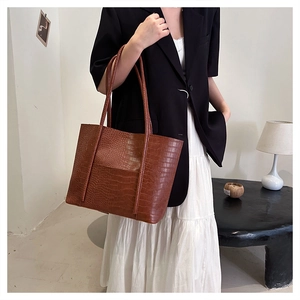 Detail of a brown tote bag with crocodile embossing and long shoulder strap