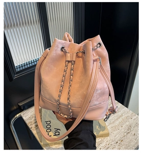 Pink drawstring bucket bag with chain detail held by model in modern interior setting