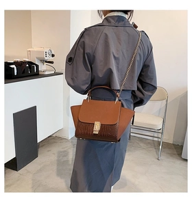 Brown leather crossbody bag with chain strap and crocodile pattern worn by a model