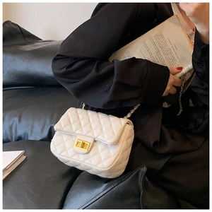 Detailed view of white quilted crossbody bag with gold chain and turn-lock on a model