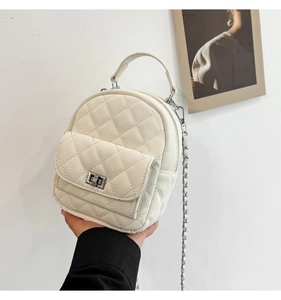 Detail of a white quilted mini backpack featuring a silver chain strap and metal twist lock