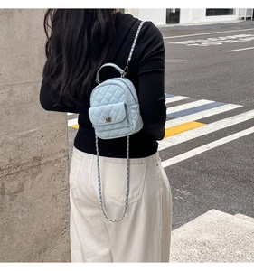 Detail view of a light blue quilted leather mini backpack with chain strap on a model