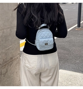 Street view of a light blue quilted mini backpack with chain strap and top handle