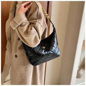 Close-up of black quilted shoulder bag featuring gold chain strap and floral logo
