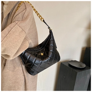 Detail view of black quilted leather hobo bag with gold chain strap on a wool coat