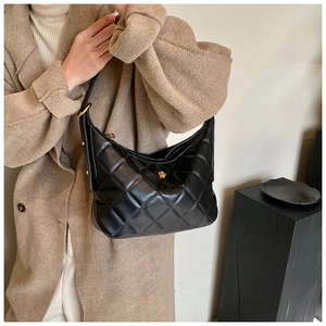Detail of black quilted shoulder bag featuring a golden camellia flower emblem and leather texture
