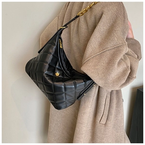 Close-up of black quilted shoulder bag with gold floral buckle and metal chain strap