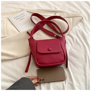 Detailed macro view of a red litchi texture leather crossbody bag with smartphone for scale
