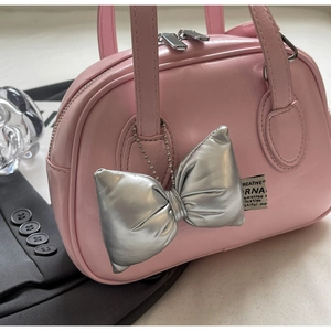 Detailansicht der rosa glänzenden Muscheltasche mit silbernem Anhänger und Stoffetikett