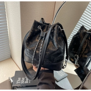 Detailed view of black bucket bag with metallic finish and dual chain straps shown in mirror