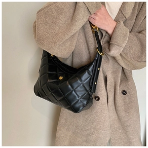 Detail of black quilted shoulder bag featuring a gold flower-shaped twist lock and hardware