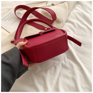 Detail of magenta lychee leather handbag featuring a crossbody strap and flap closure