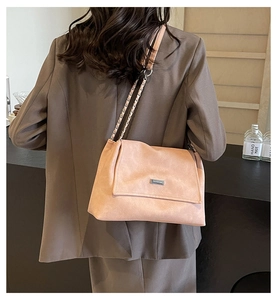 Detail of dusty pink suede shoulder bag with chain strap worn by model in a cafe