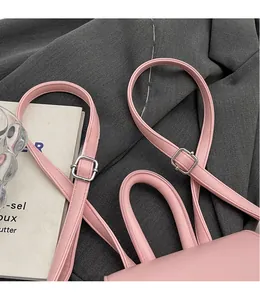 Dettaglio mini zaino rosa con spallacci regolabili e manico superiore su superficie in tessuto