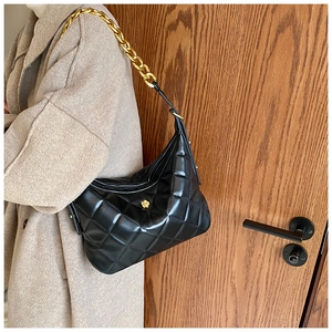 Detail of black quilted hobo bag with gold chain strap and floral logo on beige coat