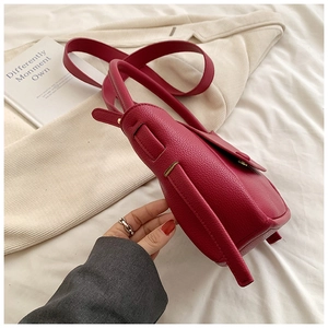 Detail view of lychee-textured faux leather handbag in rose red with golden buckle