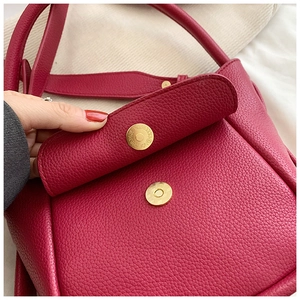 Detail of lychee textured leather texture and golden magnetic closure on dark red handbag