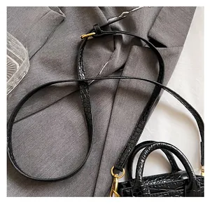 Detail of black crocodile texture mini bag with gold hardware on a grey suit jacket