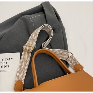 Detail einer braunen Lederhandtasche mit einem gewebten Schultergurt mit Geometriemuster