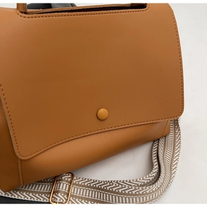 Detail der karamellbraunen Kunstledertasche mit Schnalle und geometrischem Webgurt