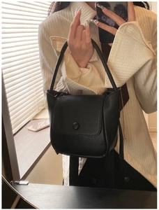 Detailed mirror view of black lychee textured leather handbag with round buckle