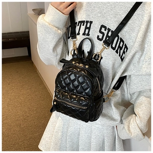 Detail of black quilted mini backpack with gold zippers and decorative bow on model