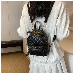 Mini black quilted backpack featuring golden hardware worn on back for size perspective