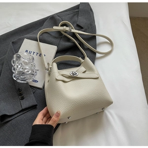 Detailaufnahme der cremefarbenen Beuteltasche mit Schleifenverschluss auf grauem Blazer