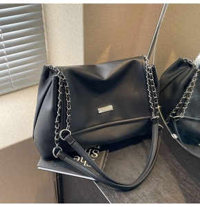 Detail of black faux leather tote with chain strap and silver logo plate on mirror