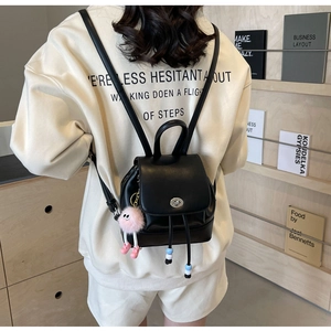 Dettaglio mini zaino in pelle nera con chiusura argentata e ciondolo a forma di bambola rosa