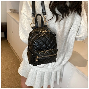 Close-up of black quilted mini backpack with golden metal zippers and textured finish