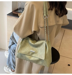 Detail of light green leather bag with silver chain strap and metal logo on beige coat