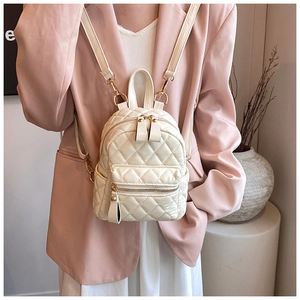 Close-up of quilted cream mini backpack with gold hardware worn by model in pink suit