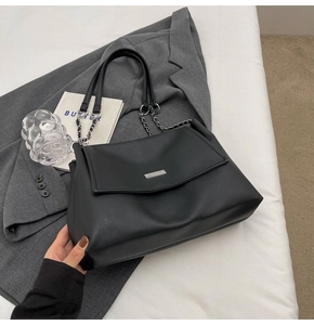 Detail of black faux leather tote bag featuring chain handle and silver logo plaque