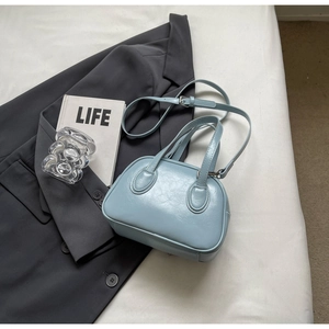 Detail der hellblauen Muscheltasche aus glänzendem PU-Leder auf grauem Blazer mit Silberteilen