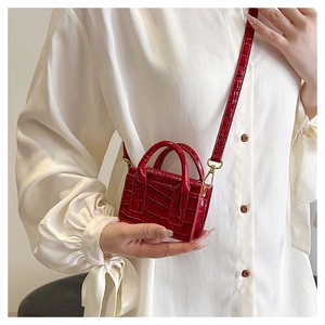 Close-up of a mini red crocodile pattern crossbody bag with tiny top handles and long strap