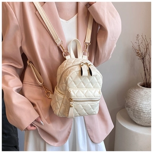 Detailed side view of a cream quilted mini backpack worn with a pink blazer and white skirt