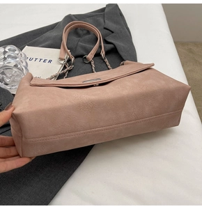 Close-up of pink suede tote bag with metal chain strap and flap closure on a minimalist table
