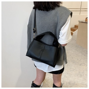 Black leather crossbody bag with pebble texture and vertical stitching on minimalist model
