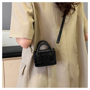 Detail of a mini black faux crocodile leather crossbody bag shown on a person