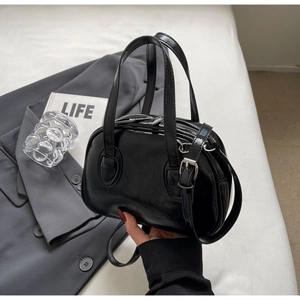 Nahaufnahme der schwarzen Lacktasche auf grauem Blazer mit minimalistischen Lifestyle-Elementen