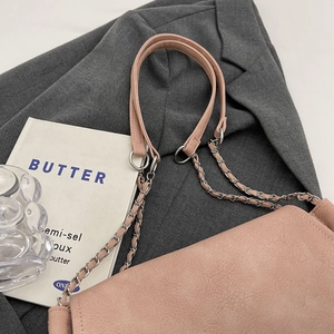 Detail of soft pink leather tote bag with chain strap on a grey blazer backdrop