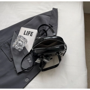 Detail der schwarzen Lackleder-Handtasche mit silbernem Schleifenanhänger und zwei Griffen