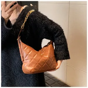 Detail of brown quilted bag with gold chain strap and rivet trim held by a model