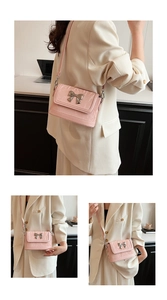 Detail of pink crossbody bag featuring metal bow decor and soft pleated leather texture