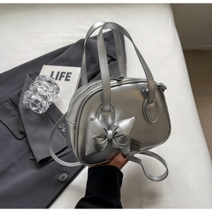 Nahaufnahme einer silbernen Muschel-Tasche mit Metallic-Finish und modischem Schleifenanhänger