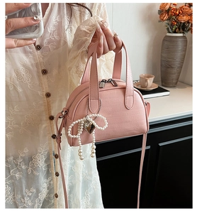 Sac à main rose à motif crocodile avec nœud en perles et breloque cœur tenu à la main