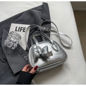 Nahaufnahme einer silbernen Metallic-Tasche mit Schleife und verstellbarem Schultergurt